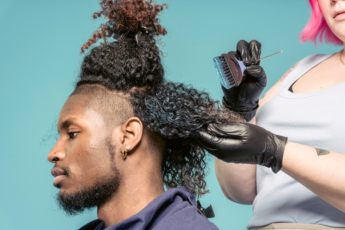 Professional hairstylist applying hair dye on curls of black client