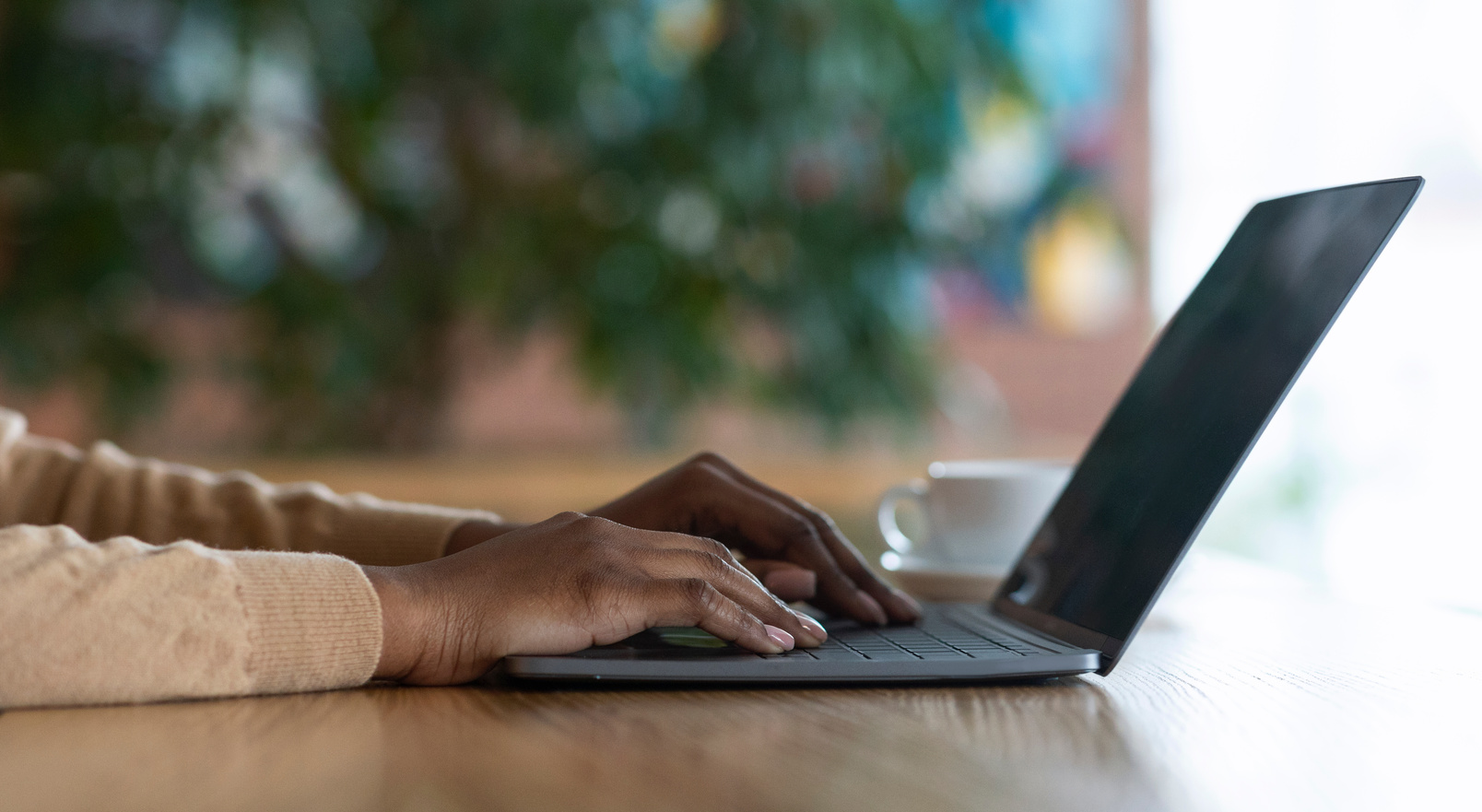Hands of black girl typing on laptop keyboard, cafe interior